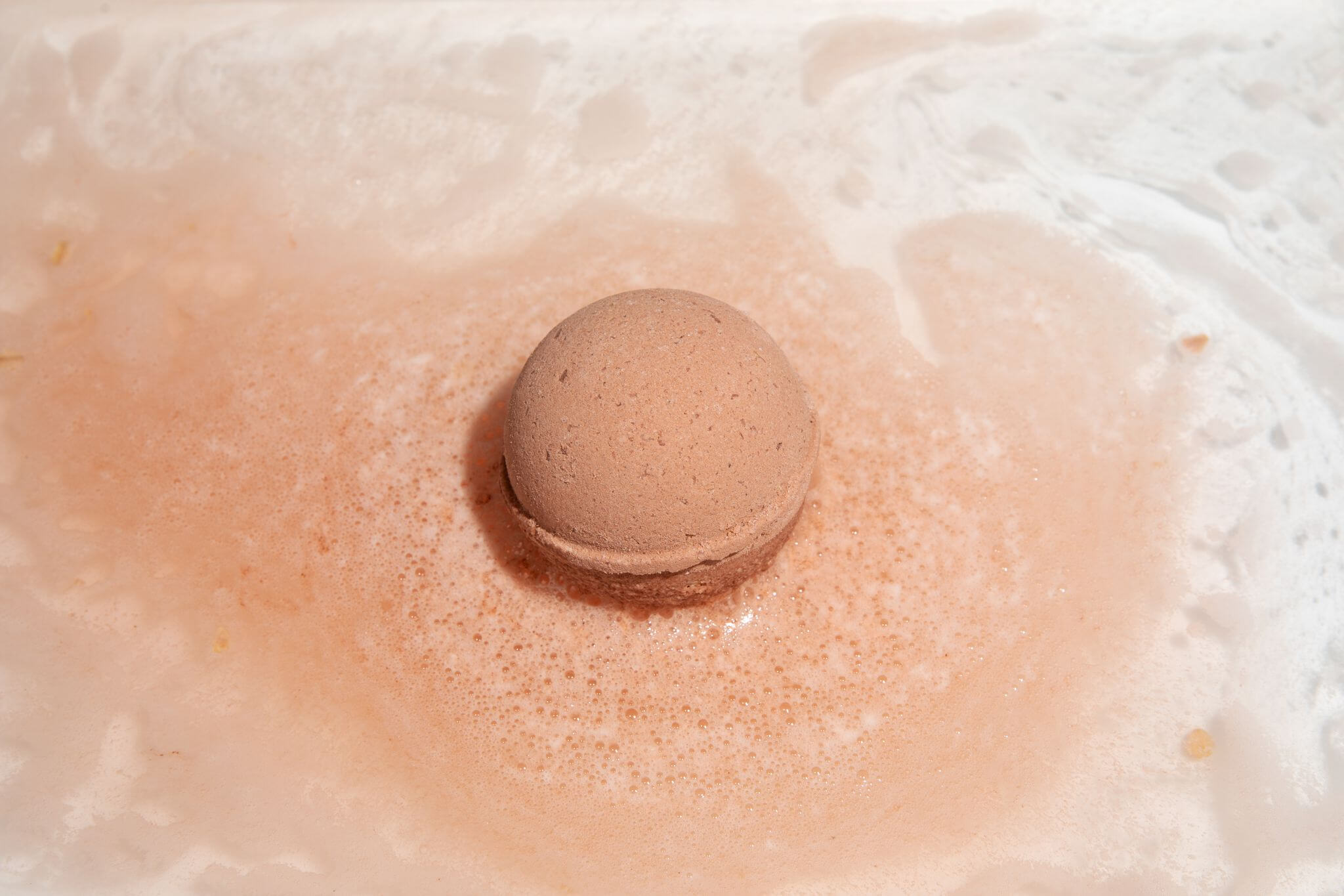 Tub Therapy | Vanilla Sandalwood CBD bath bomb fizzing in water, turning it into a soft mocha brown color.